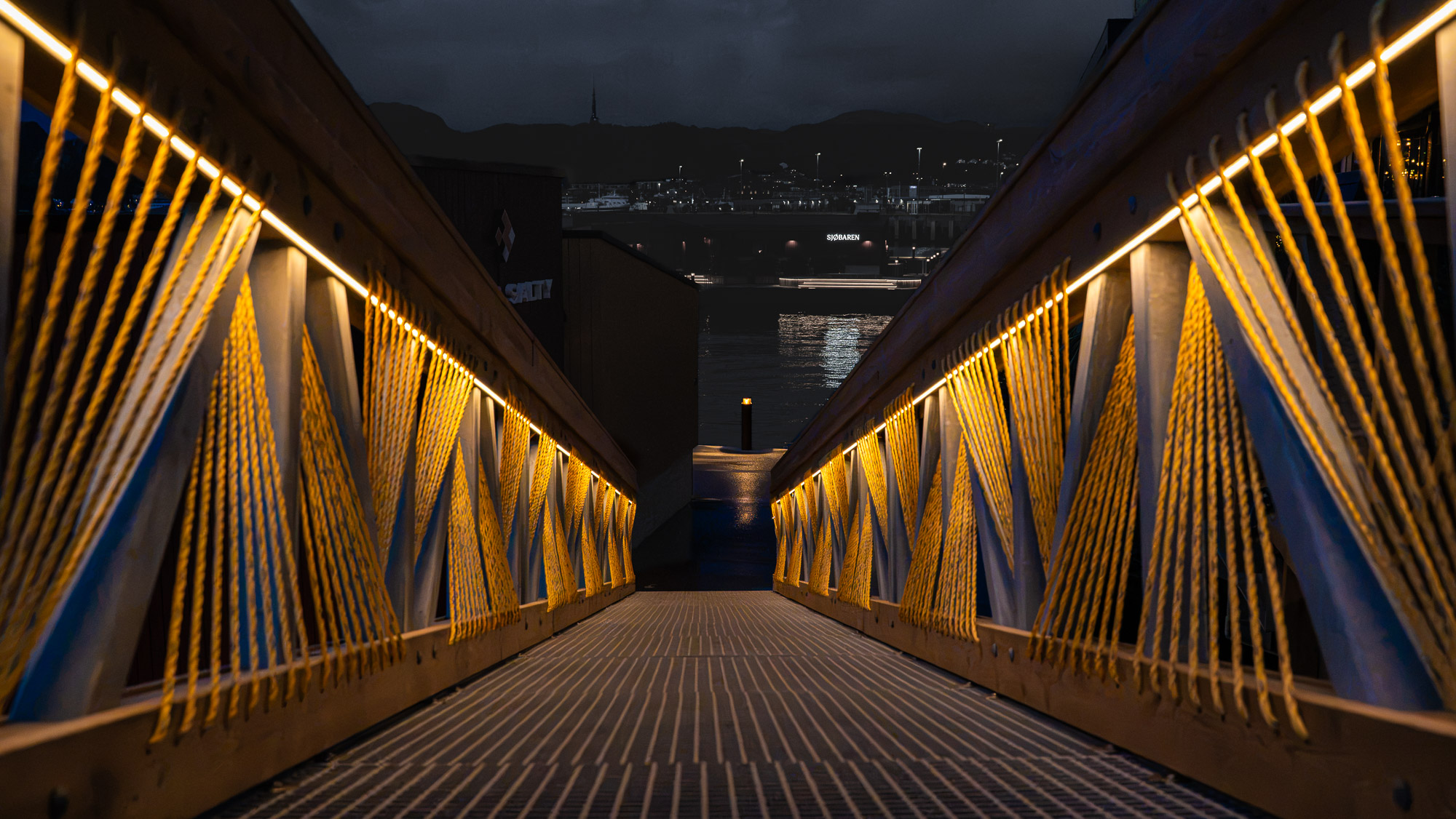 The Sunweave gangway at night, with rope and a strip of light along both handrails, looking out over the fjord